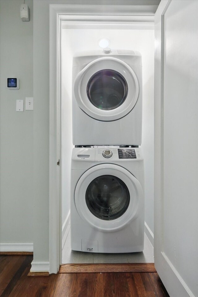 clothes washing area featuring stacked washer / drying machine, wood finished floors, and baseboards