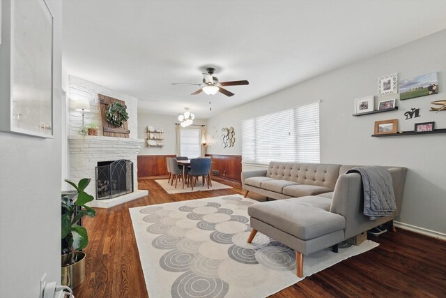 living area featuring ceiling fan, wood finished floors, a brick fireplace, and a wainscoted wall