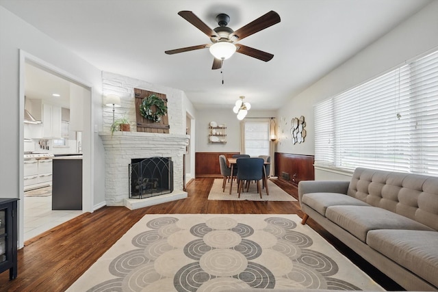 living room with wood finished floors, a ceiling fan, wainscoting, and a fireplace
