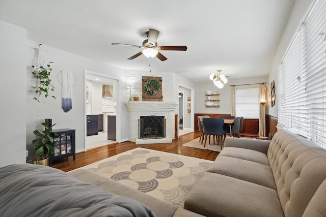 living room with a ceiling fan, wood finished floors, a brick fireplace, and a chandelier