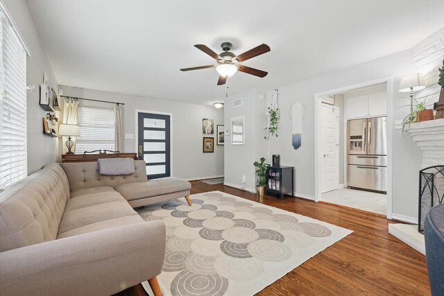 living area with ceiling fan, wood finished floors, a fireplace with raised hearth, and baseboards