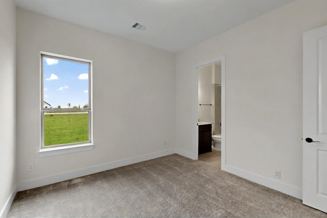unfurnished bedroom featuring light colored carpet, baseboards, and ensuite bathroom