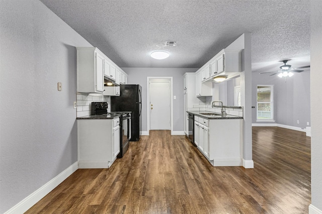 kitchen with black appliances, a sink, under cabinet range hood, baseboards, and a textured ceiling