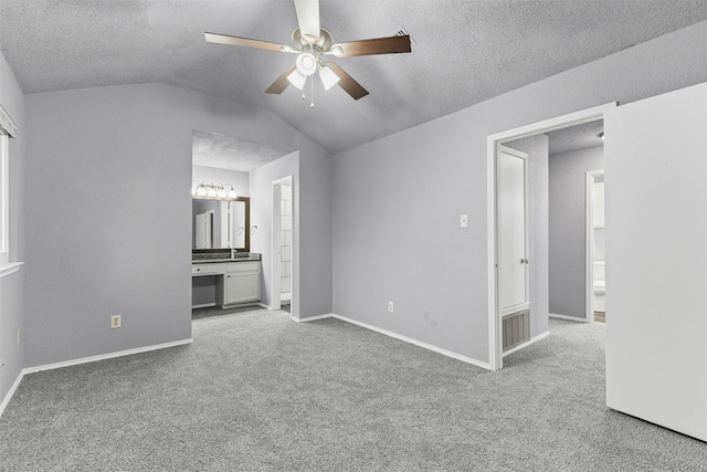 unfurnished bedroom featuring lofted ceiling, carpet floors, a textured ceiling, baseboards, and ensuite bath