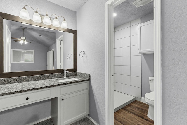 bathroom with a textured wall, toilet, wood finished floors, vanity, and ceiling fan