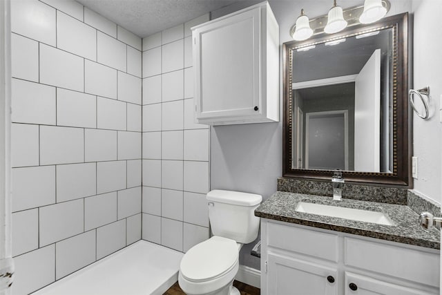 full bath with toilet, vanity, tiled shower, baseboards, and a textured ceiling