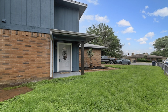entrance to property featuring brick siding and a lawn