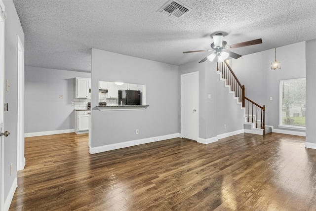 unfurnished living room featuring dark wood-style flooring, ceiling fan, a textured ceiling, stairs, and baseboards