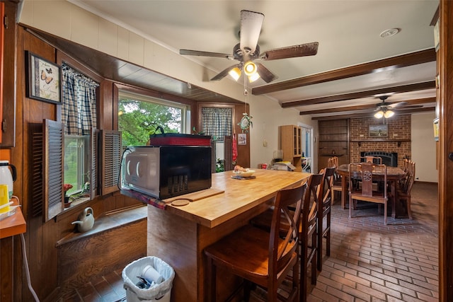 201 Sunset Dr, Fairfield, TX 75840 - dining space with ceiling fan, brick flooring, a fireplace, beam ceiling, and wood walls