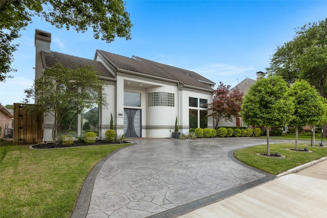 view of front facade featuring a chimney, curved driveway, stucco siding, a front yard, and a tile roof