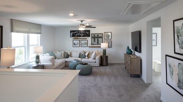 carpeted living area featuring attic access, ceiling fan, and baseboards