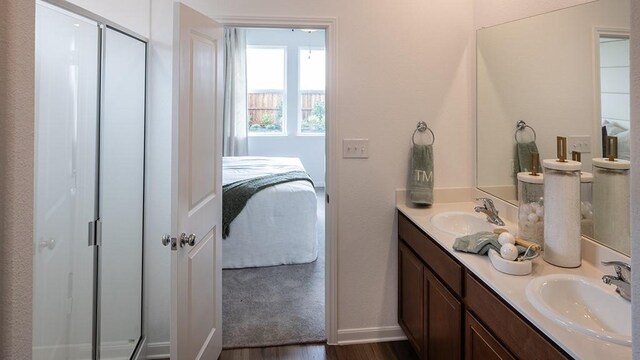 full bath featuring connected bathroom, wood finished floors, double vanity, a shower with shower door, and baseboards