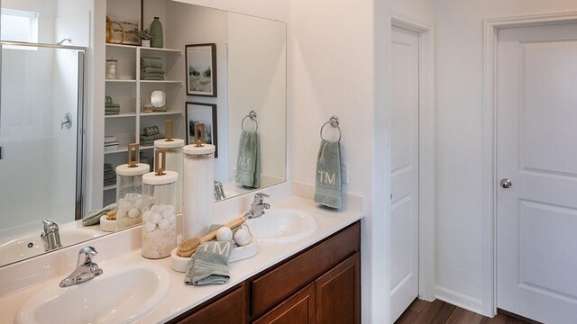 full bath featuring a shower stall, double vanity, and wood finished floors