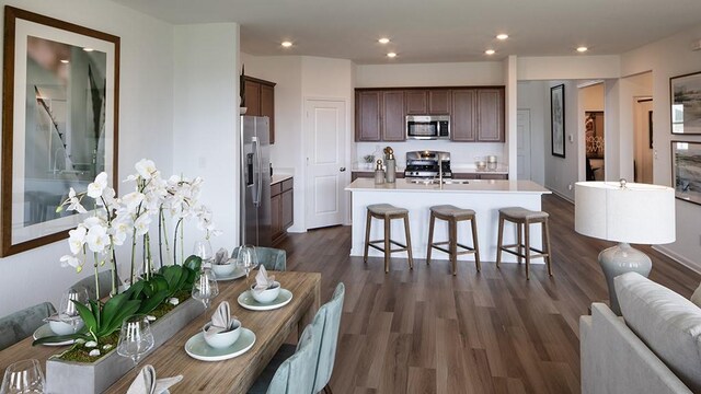 kitchen featuring stainless steel appliances, light countertops, an island with sink, dark wood-style flooring, and a sink