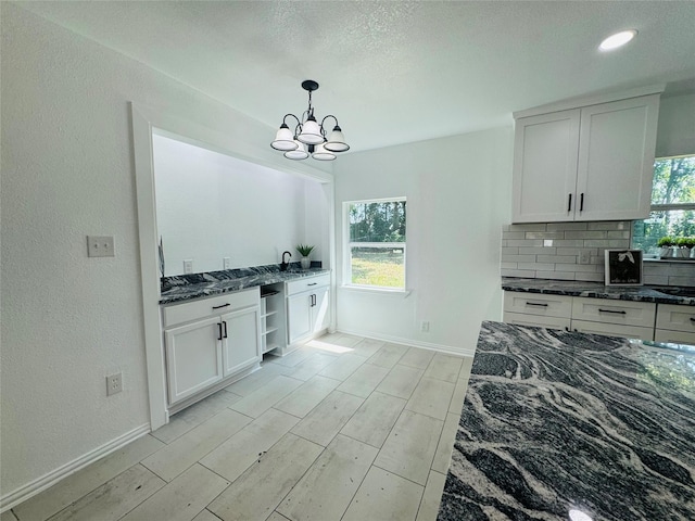 2719 S 27th, Waco, TX 76706 - kitchen featuring dark stone counters, tasteful backsplash, a chandelier, white cabinets, and a textured wall