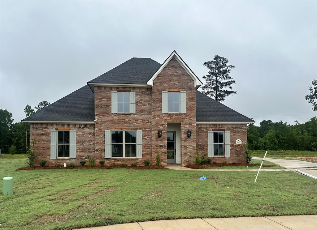 view of front of house with a shingled roof, brick siding, and a front yard