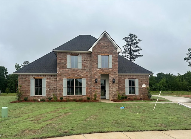 view of front of house with a shingled roof, brick siding, and a front yard
