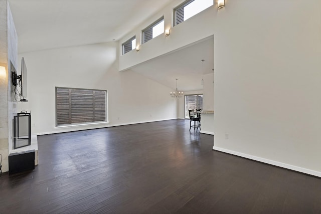 unfurnished living room with a chandelier, dark wood finished floors, high vaulted ceiling, and baseboards