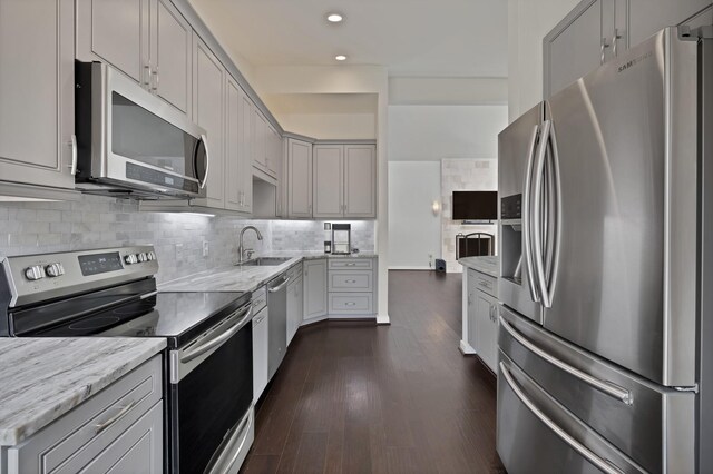 kitchen with appliances with stainless steel finishes, a sink, dark wood-type flooring, recessed lighting, and light stone countertops