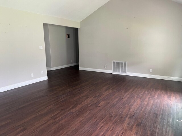 spare room featuring dark wood-type flooring, baseboards, and high vaulted ceiling