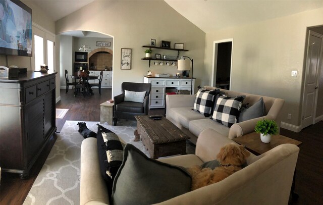 living area with arched walkways, vaulted ceiling, dark wood-style floors, and baseboards