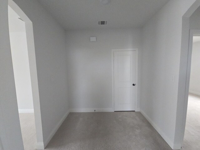 empty room with light colored carpet, baseboards, and arched walkways