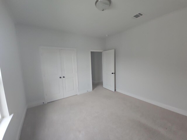 unfurnished bedroom featuring a closet, light colored carpet, and baseboards