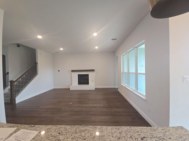 unfurnished living room with wood finished floors, a brick fireplace, recessed lighting, baseboards, and stairs