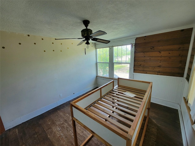 1208 W Broadway, Clarksville, TX 75426 - unfurnished bedroom with wood-type flooring, a textured ceiling, baseboards, wood walls, and a ceiling fan