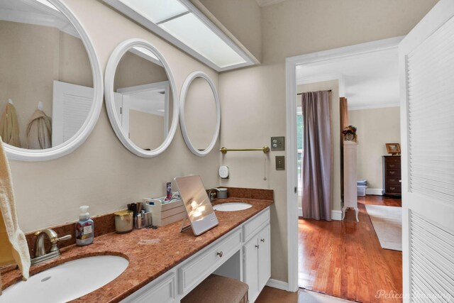 bathroom with wood finished floors, double vanity, ornamental molding, and baseboards