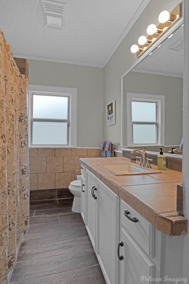 full bathroom featuring toilet, ornamental molding, vanity, wainscoting, and wood finished floors