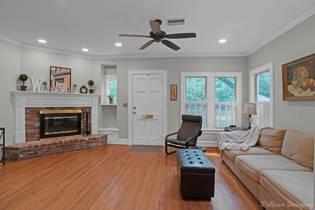 living room with wood finished floors, a ceiling fan, a fireplace, ornamental molding, and recessed lighting