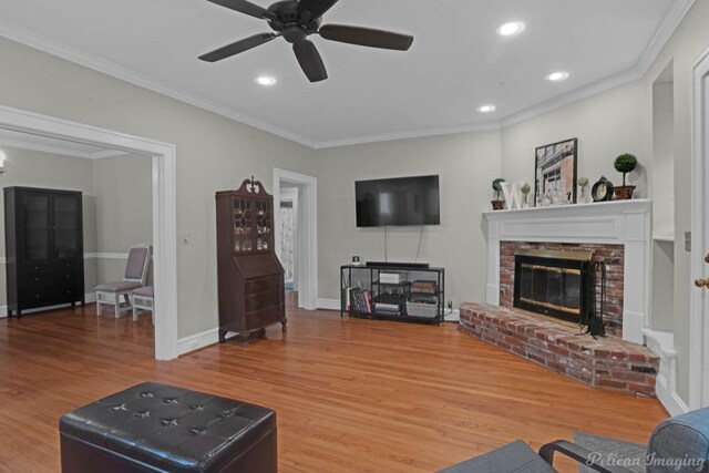 living area with wood finished floors, a brick fireplace, crown molding, recessed lighting, and a ceiling fan