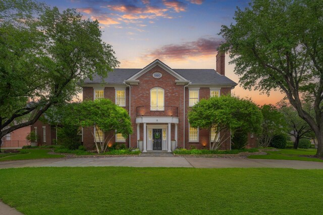 colonial inspired home with a chimney, a yard, and brick siding