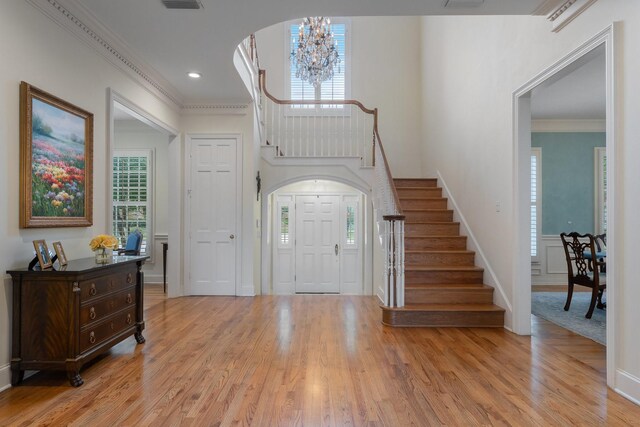foyer with a chandelier, stairway, healthy amount of natural light, light wood-style flooring, and crown molding