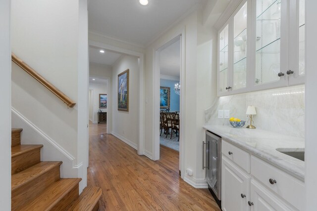 indoor dry bar featuring ornamental molding, stairs, beverage cooler, light wood finished floors, and backsplash