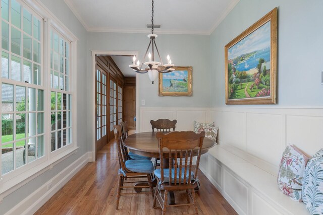 dining space featuring wood finished floors, healthy amount of natural light, a chandelier, ornamental molding, and wainscoting