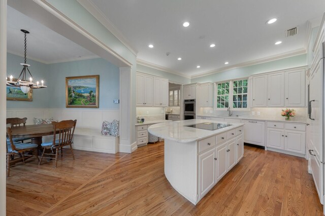 kitchen with paneled dishwasher, a sink, ornamental molding, a chandelier, and a kitchen island