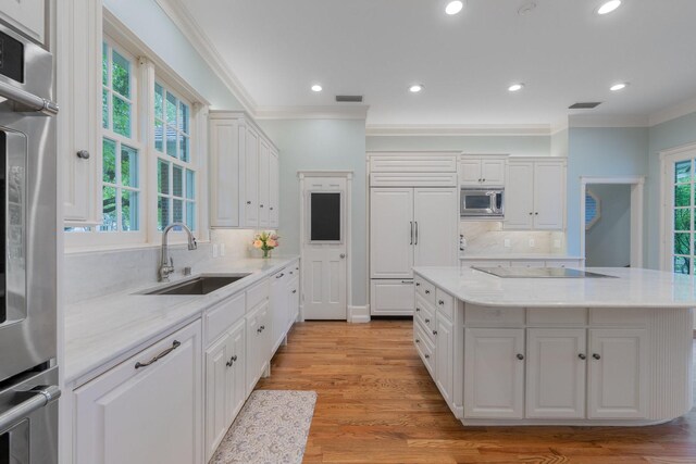 kitchen with built in appliances, a sink, ornamental molding, healthy amount of natural light, and white cabinetry