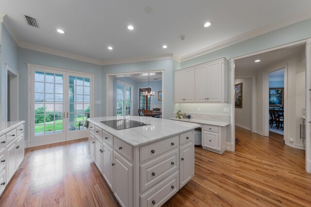 kitchen featuring black electric stovetop, light wood finished floors, white cabinets, ornamental molding, and a kitchen island
