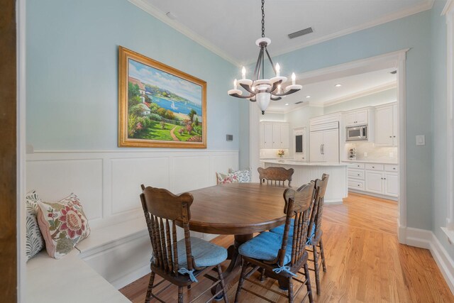 dining room with a chandelier, ornamental molding, light wood-style floors, and a wainscoted wall