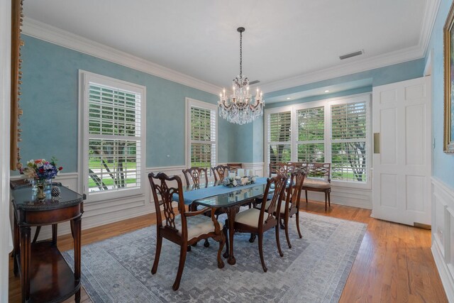 dining area featuring a chandelier, a wainscoted wall, plenty of natural light, ornamental molding, and wood finished floors