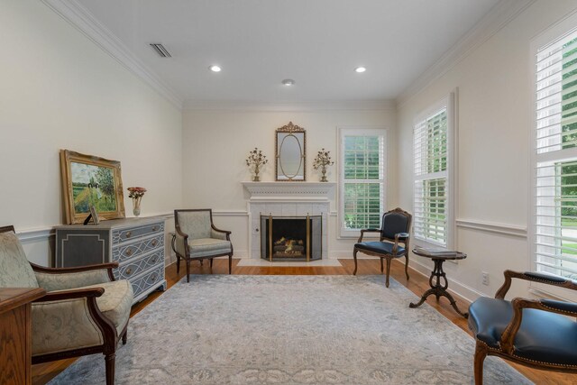 living area with wood finished floors, ornamental molding, a tile fireplace, recessed lighting, and baseboards