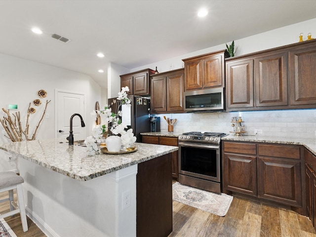 1111 Burlingame Dr, Cleburne, TX 76033 - kitchen with stainless steel appliances, tasteful backsplash, a kitchen breakfast bar, wood finished floors, and light stone countertops