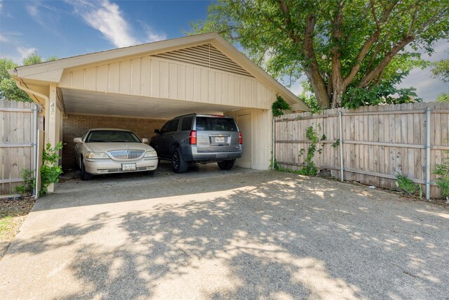 view of parking / parking lot with concrete driveway, fence, and a carport