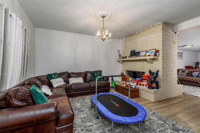 living area featuring wood finished floors, a chandelier, and a brick fireplace