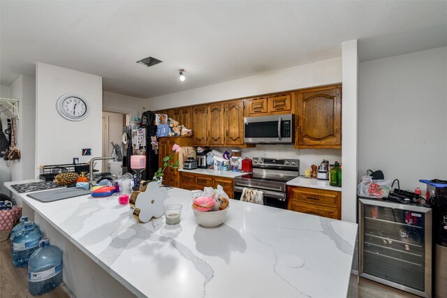 kitchen with stainless steel appliances, beverage cooler, brown cabinetry, and wood finished floors