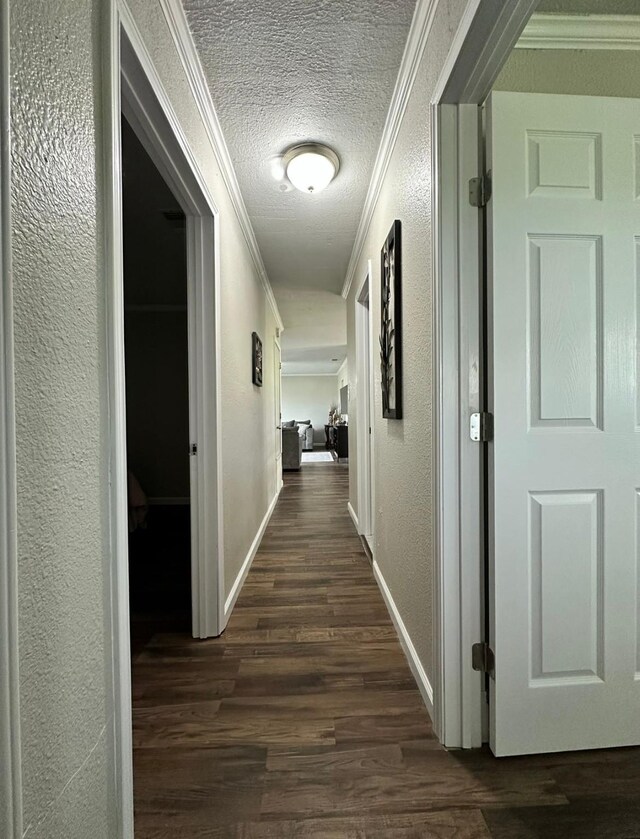 corridor with ornamental molding, dark wood finished floors, a textured wall, a textured ceiling, and baseboards