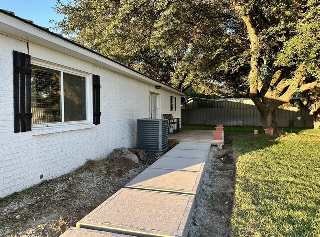 view of side of home with brick siding, central AC, a deck, and a yard