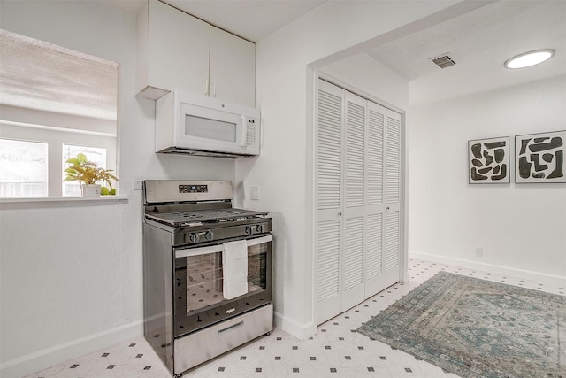 kitchen featuring gas range, white microwave, white cabinetry, light flooring, and baseboards